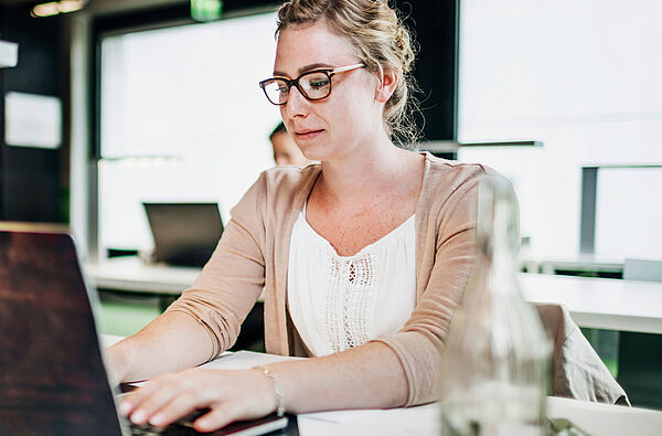 Junge Frau sitzt am Laptop. Sie hat die Hände auf der Tastatur.