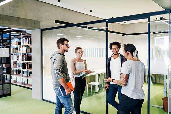 Mehreren jungen Menschen wird in der Bibliothek etwas erkklärt.
