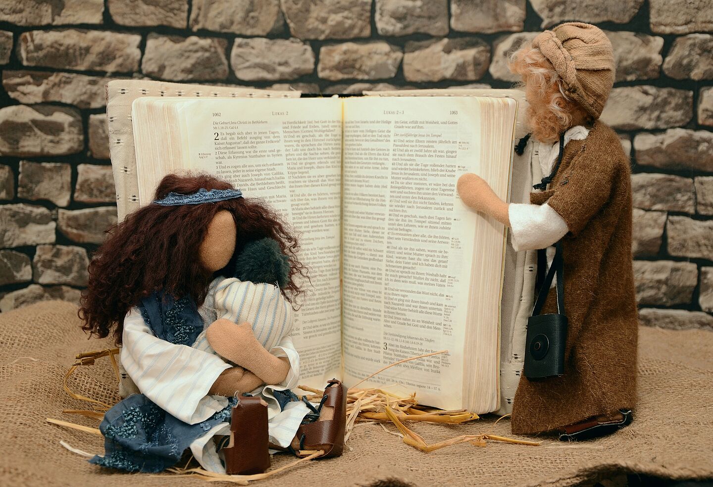 Puppen illustrieren die Geburt Jesu. Die kleine Familie steht vor einem geöffneten Buch.