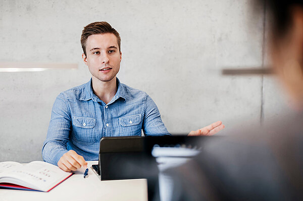 Am Tisch sitzender Student mit aufgeschlagenem Buch vor sich