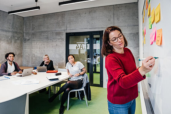 Eine Frau erklärt Studierenden etwas an der Wandtafel